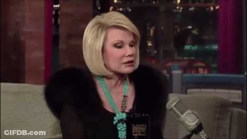 Woman On Couch Talking Into Microphone In Fur Coat And Turquoise Necklace GIF