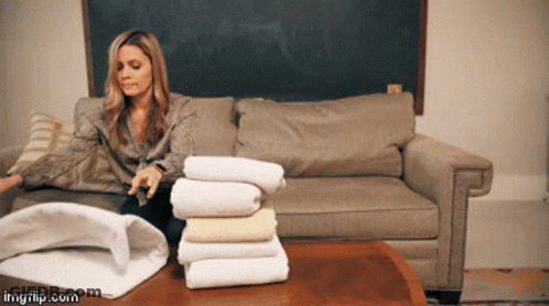 Woman On Couch With Stack Of Towels On Table GIF