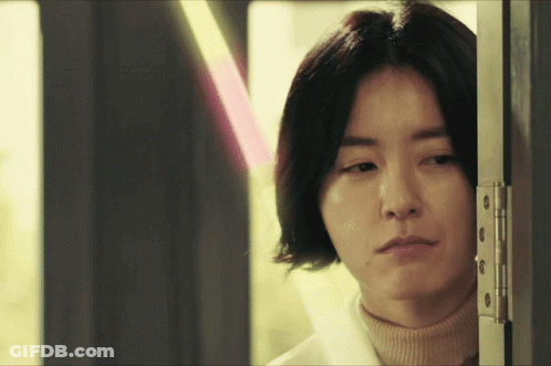 Woman Peeking Behind Door In Turtleneck GIF