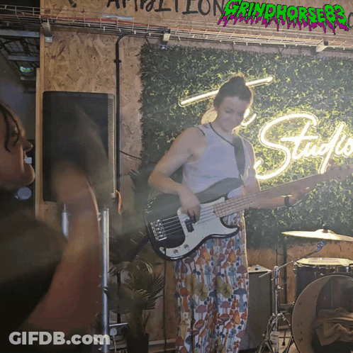 Woman Playing Bass Guitar In Front Of Grindhouse Sign GIF
