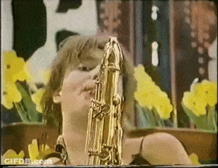 Woman Playing Saxophone In Front Of Yellow Flowers GIF