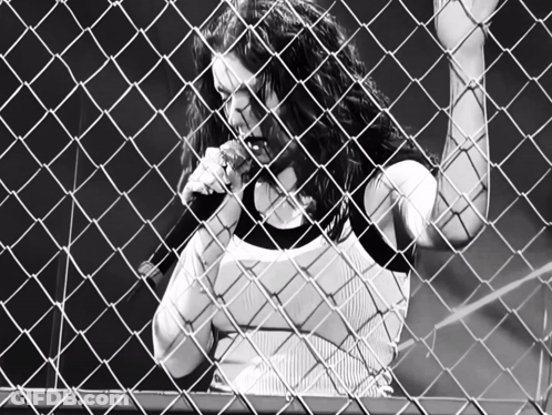 Woman Singing Behind Chain Link Fence With Letter C GIF