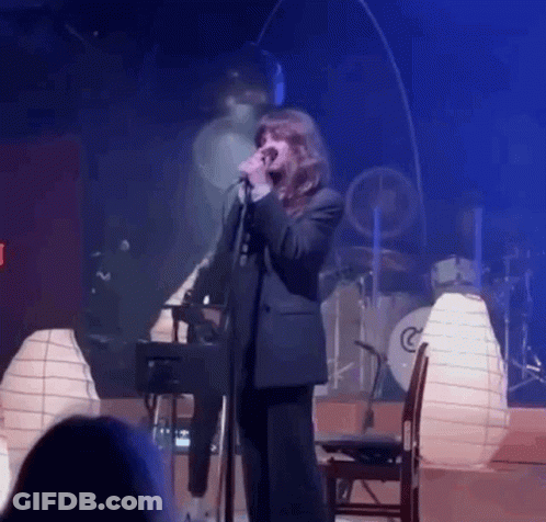Woman Singing Into Microphone With Drum Set GIF