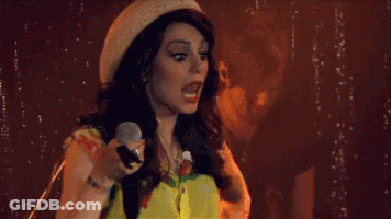 Woman Singing Into Microphone With Hat And Yellow Shirt GIF