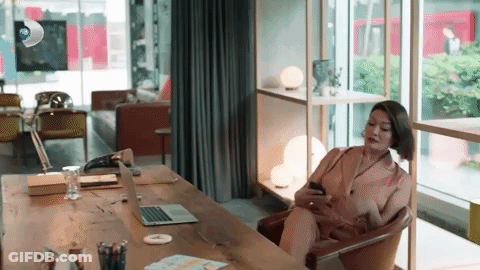 Woman Sitting At Desk With Laptop And Cell Phone GIF
