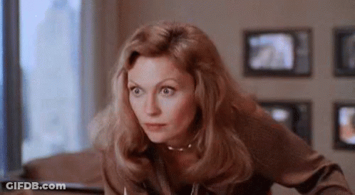 Woman Sitting At Table In Front Of TV Looking At Camera GIF