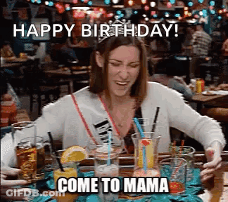 Woman Sitting At Table With Drinks And Happy Birthday Come To Mama Sign GIF