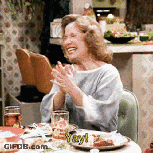 Woman Sitting At Table With Food And Yay Sign GIF