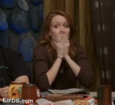 Woman Sitting At Table With Hands Up And Funny Face GIF