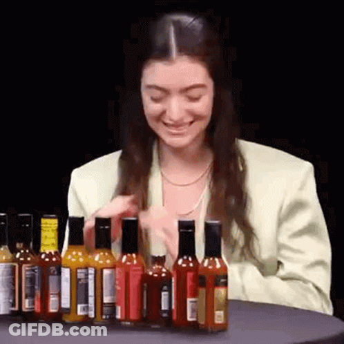 Woman Sitting At Table With Hot Sauce Bottles GIF