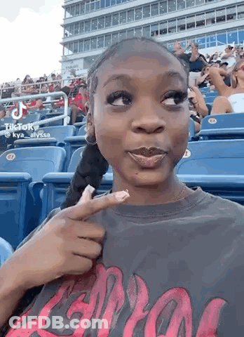 Woman Sitting In Baseball Stands Pointing At Face GIF