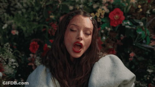 Woman Sitting In Field Of Flowers With Red Lipstick GIF