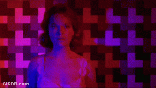 Woman Sitting In Front Of Checkered Wall With Purple And Red Lights GIF