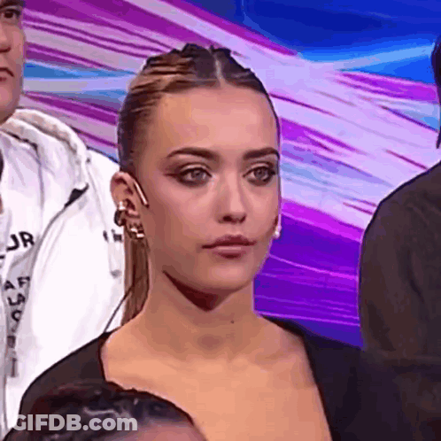 Woman Sitting In Front Of Crowd Looking At Camera GIF