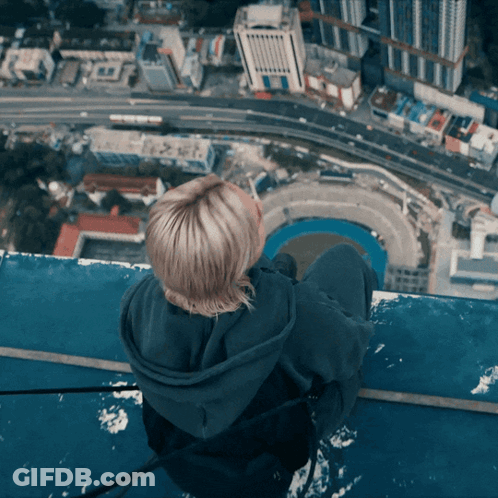 Woman Sitting On Building Edge Overlooking City GIF