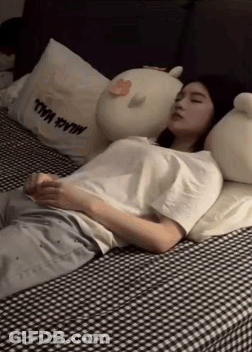 Woman Sleeping On Bed With Stuffed Animals And Black Wall Pillow GIF