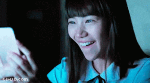 Woman Smiling At Phone In Dark GIF