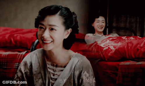 Woman Smiling In Front Of Picture Of Woman On Bed With Red Blanket GIF