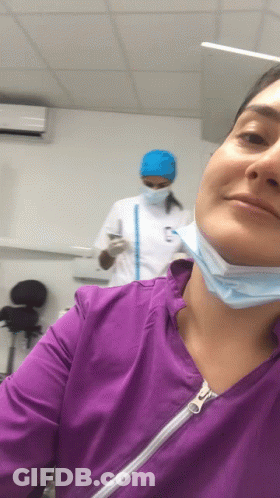 Woman Smiling In Purple Scrub Top And Face Mask GIF