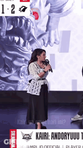 Woman Speaking Into Microphone In Front Of Kairi Andoryuu Poster GIF