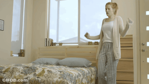 Woman Standing By Bed With Floral Comforter GIF