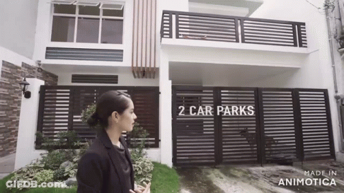 Woman Standing In Front Of House With Fence And Car Park GIF