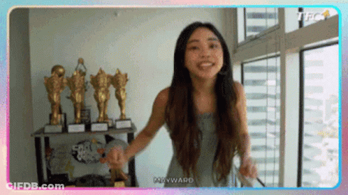 Woman Standing In Front Of Window With Trophies GIF