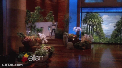 Woman Standing In Room With Flowers And Word Ellen GIF