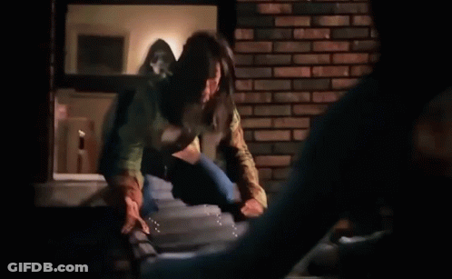Woman Standing On Ledge Next To Brick Wall In Dark Room GIF