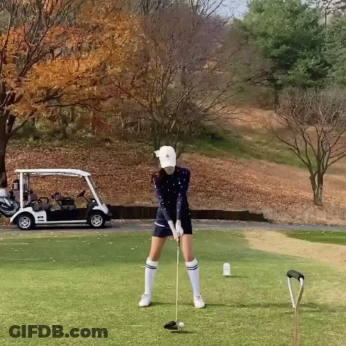 Woman Swinging Golf Club With Golf Cart In Background GIF