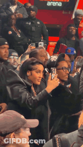 Woman Taking Picture Of Man In Front Of Arena GIF