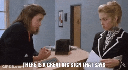 Woman Talking To Another Woman There Is A Great Big Sign That Says GIF