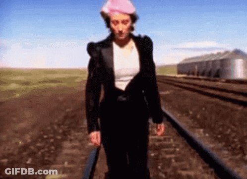Woman Walking Train Tracks Wearing Hat GIF