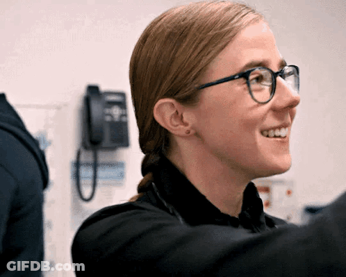 Woman Wearing Glasses And Black Shirt Smiling In Front Of Telephone GIF