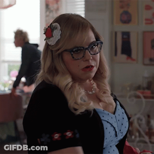Woman Wearing Glasses And Flower In Hair Stands In Room GIF