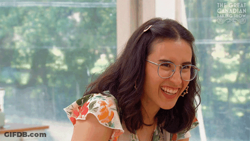 Woman Wearing Glasses Smiling In Front Of Great Canadian Baking Show GIF