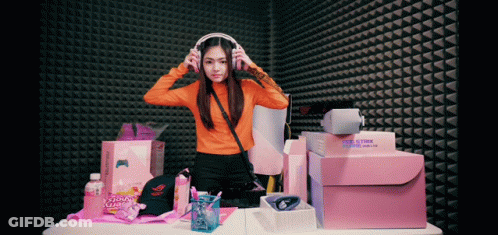 Woman Wearing Headphones In Front Of Gamer Hat And Boxes GIF
