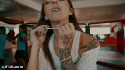 Woman With Arm Tattoo Holding Something In Mouth GIF