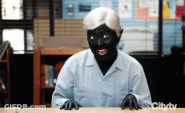 Woman With Black Face And White Hair Sitting At Table GIF