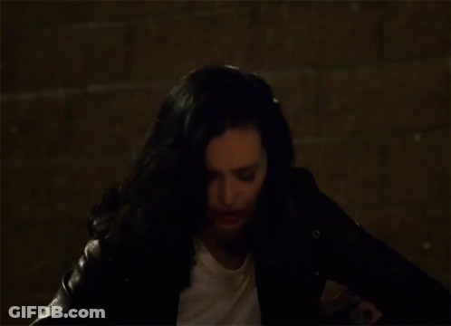 Woman With Black Hair And White Shirt Sitting In Dark Room GIF