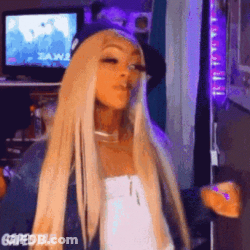 Woman With Blonde Hair And Purple Hat Standing In Front Of Television GIF