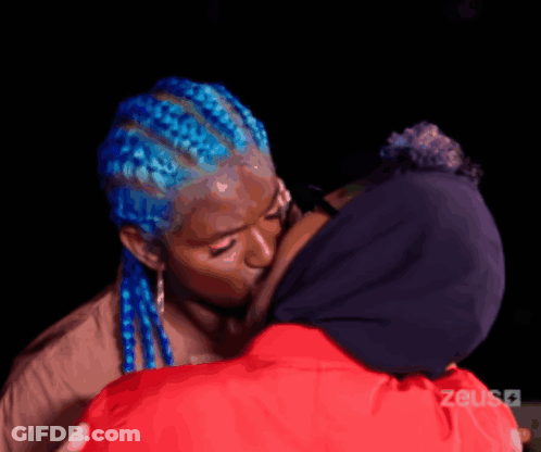 Woman With Blue Braids Kissing Woman In Red Jacket GIF