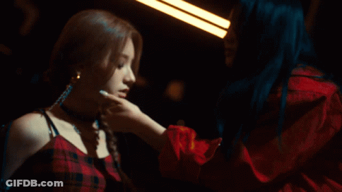 Woman With Blue Hair Touching Another Woman's Face In Dark Room GIF