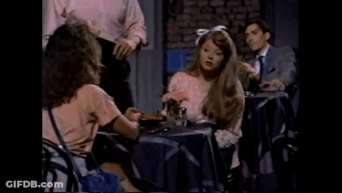 Woman With Bow In Hair Sitting At Table With Flowers And Man GIF