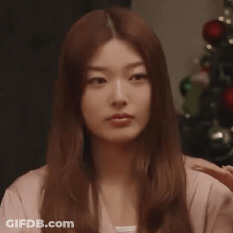 Woman With Brown Hair By Christmas Tree Looking At Camera GIF