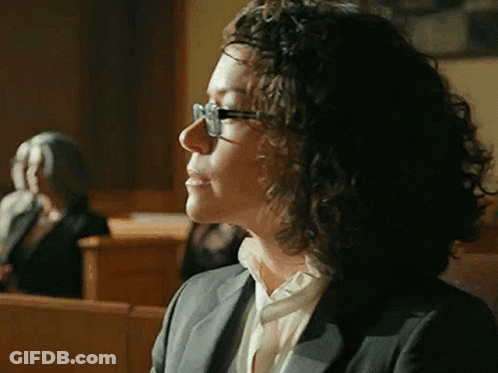 Woman With Curly Hair And Glasses Sitting In Courtroom GIF