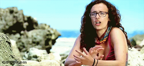 Woman With Curly Hair And Glasses Sitting On Beach GIF