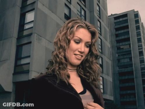 Woman With Curly Hair In Front Of Tall Building GIF