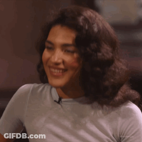 Woman With Curly Hair In Light Blue Shirt Smiling GIF
