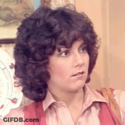 Woman With Curly Hair In Pink Shirt And Red Vest GIF